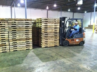Forklift operator moving stacked wood pallets in a warehouse